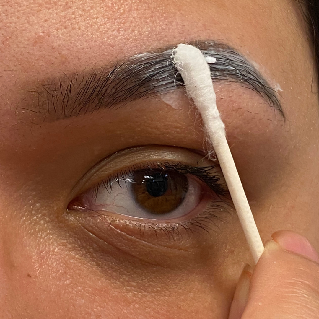 Woman applying aftercare to new brow PMU using a q-tip