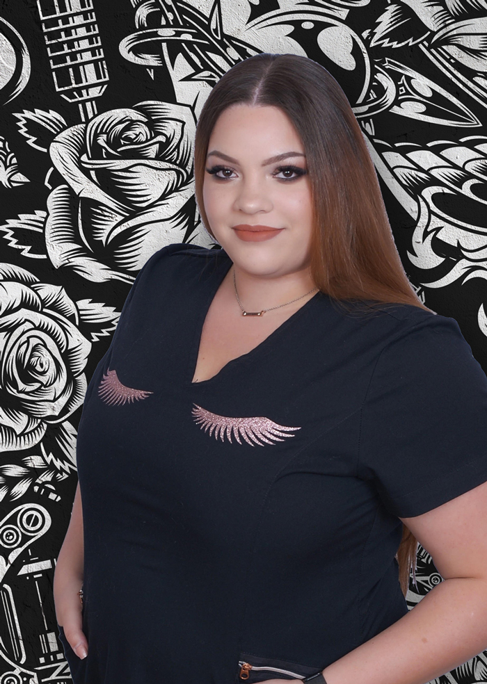 Permanent Makeup artist Jillian Silva standing with right hand on hip in front of traditional tattoo background art.