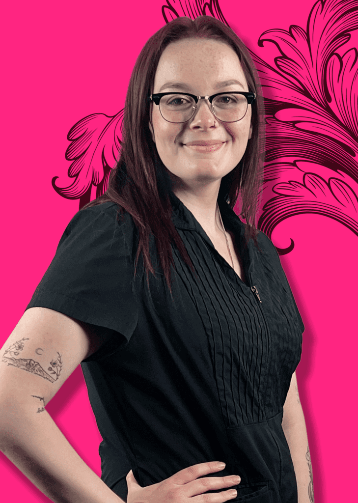 Graphic Designer and Marketer Willow standing with left hand on hip in front of traditional tattoo background art.